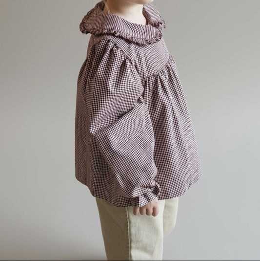 Child wearing a checkered blouse with a high collar against a plain background