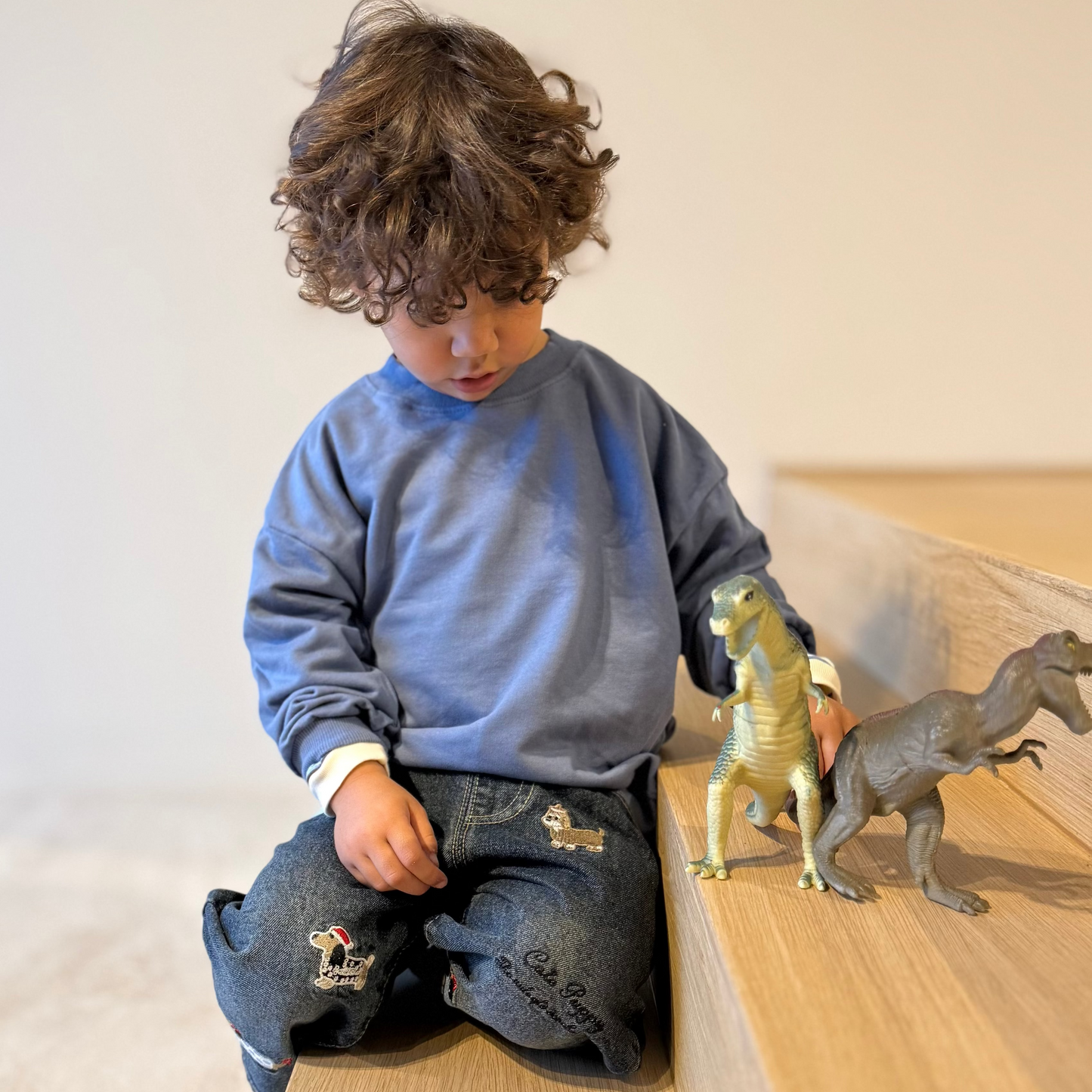 Child playing with toy dinosaurs on a wooden floor