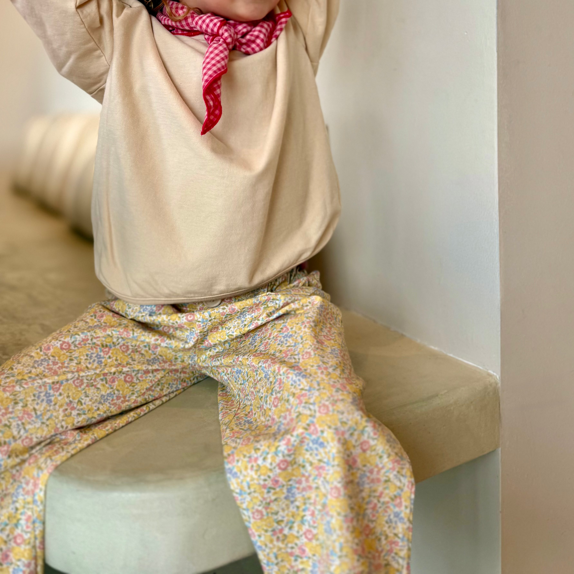Child wearing a beige hoodie and colorful pants sitting on a couch.