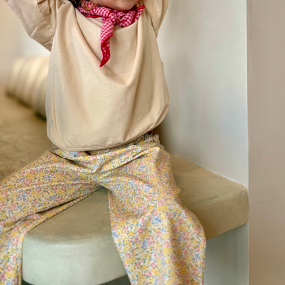 Child wearing a beige hoodie and colorful pants sitting on a couch.