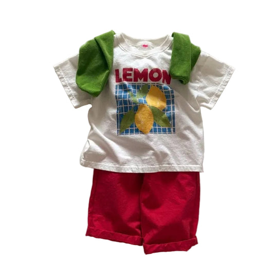 Children's outfit with a white t-shirt featuring a lemon graphic and red shorts on a light gray background.