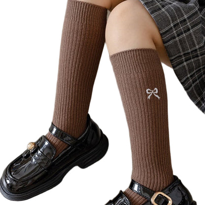 Brown knee-high socks with a bow design worn by a person sitting on the floor.