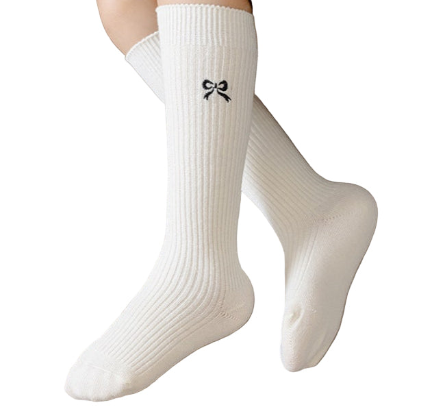 White socks with a black bow design worn by a person sitting on a beige surface.
