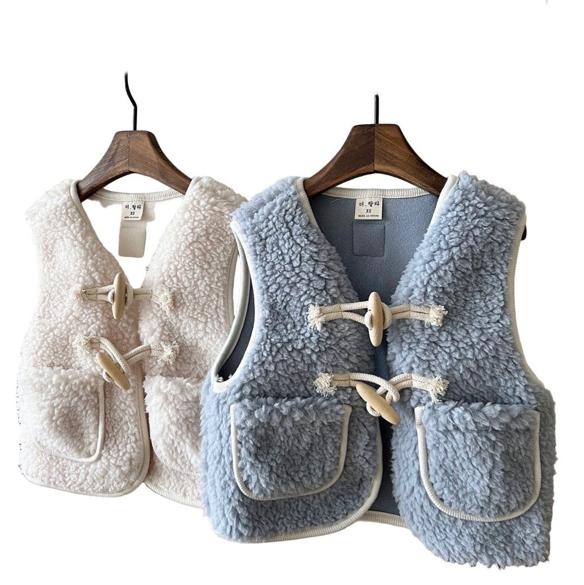 Two children's vests, one beige and one blue, on hangers against a white background.