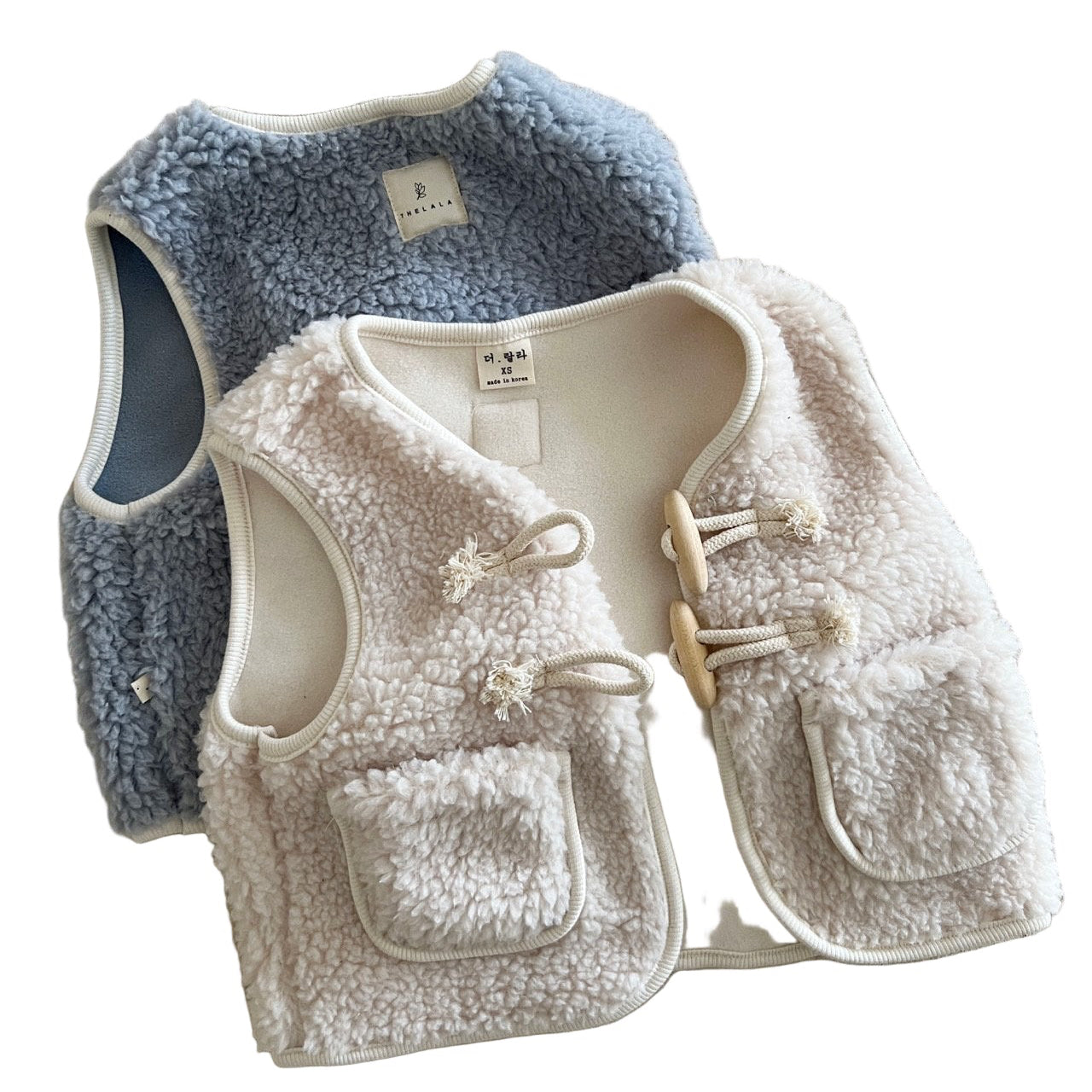 Two children's vests, one blue and one beige, on a textured surface with 'THELALA' branding.